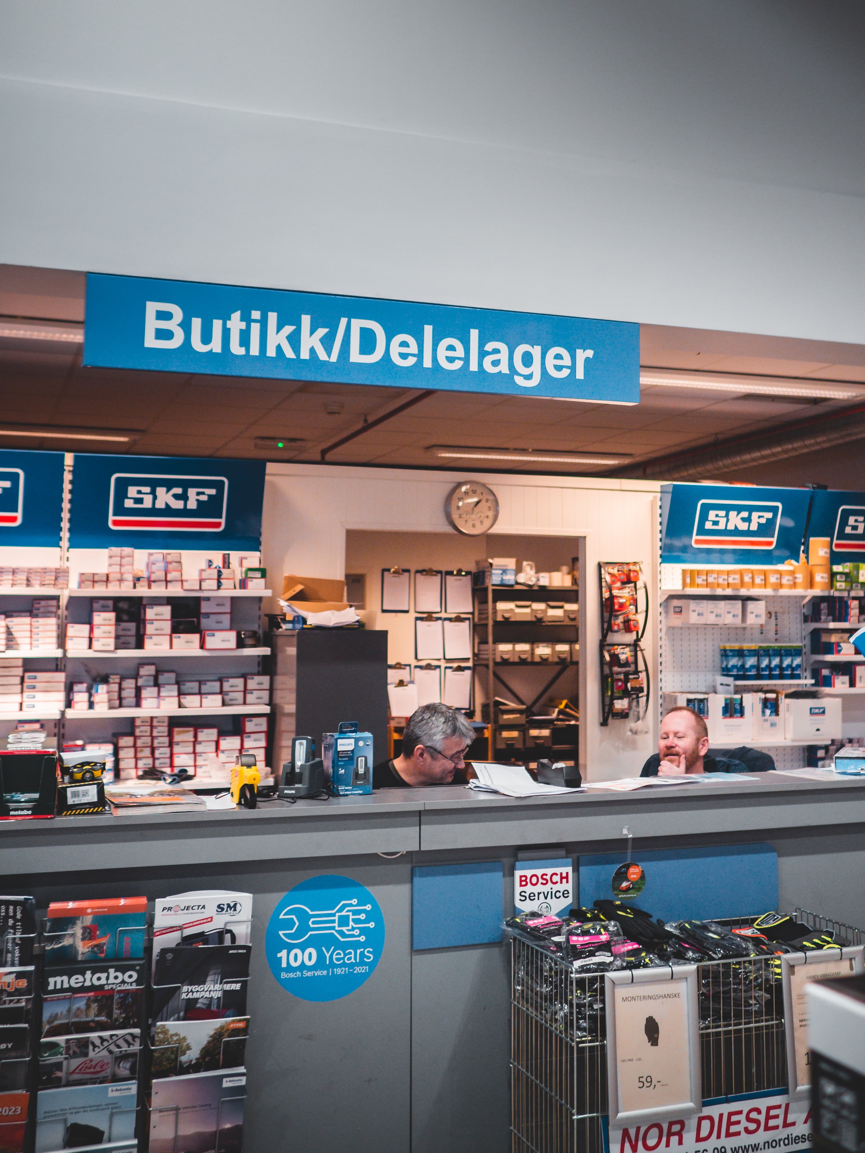 Sten-Tore, omgitt av delelager, smiler og ler med en kollega i butikkluken.